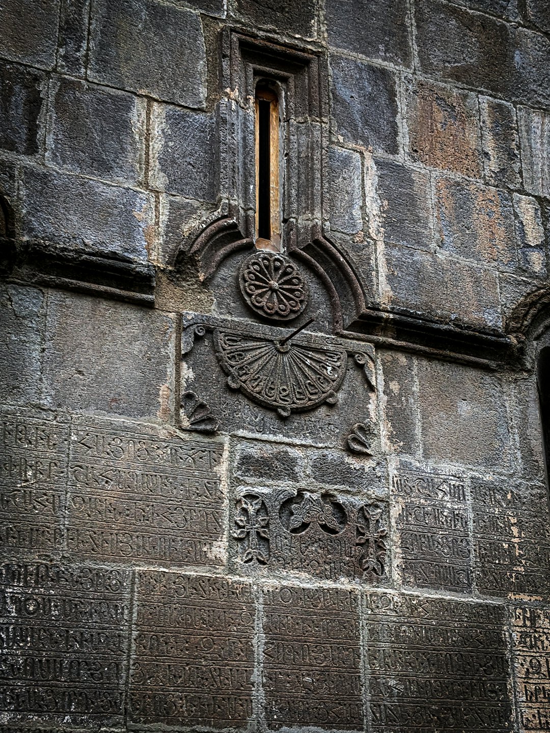 Antica muraglia di pietra con iscrizioni scolpite e una meridiana circolare.