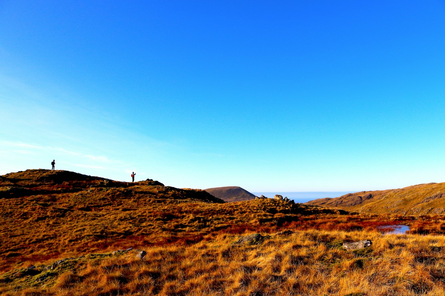 Due escursionisti stagliati su colline aride sotto un cielo blu.